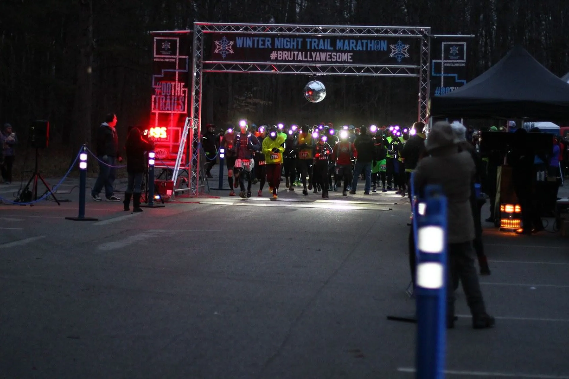 The image shows a group of runners at the start line of a night-time running