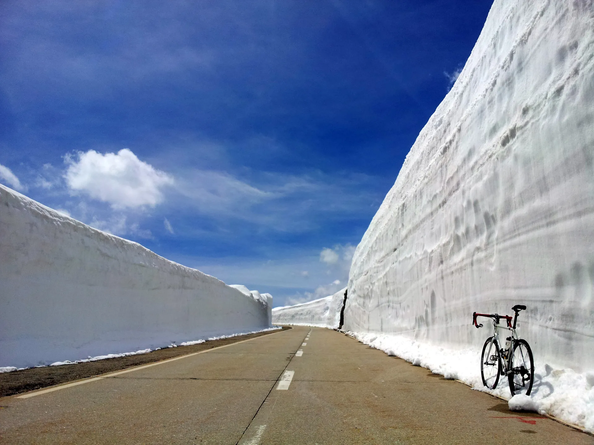 The image displays a road with extremely high walls of snow on each side, indicating