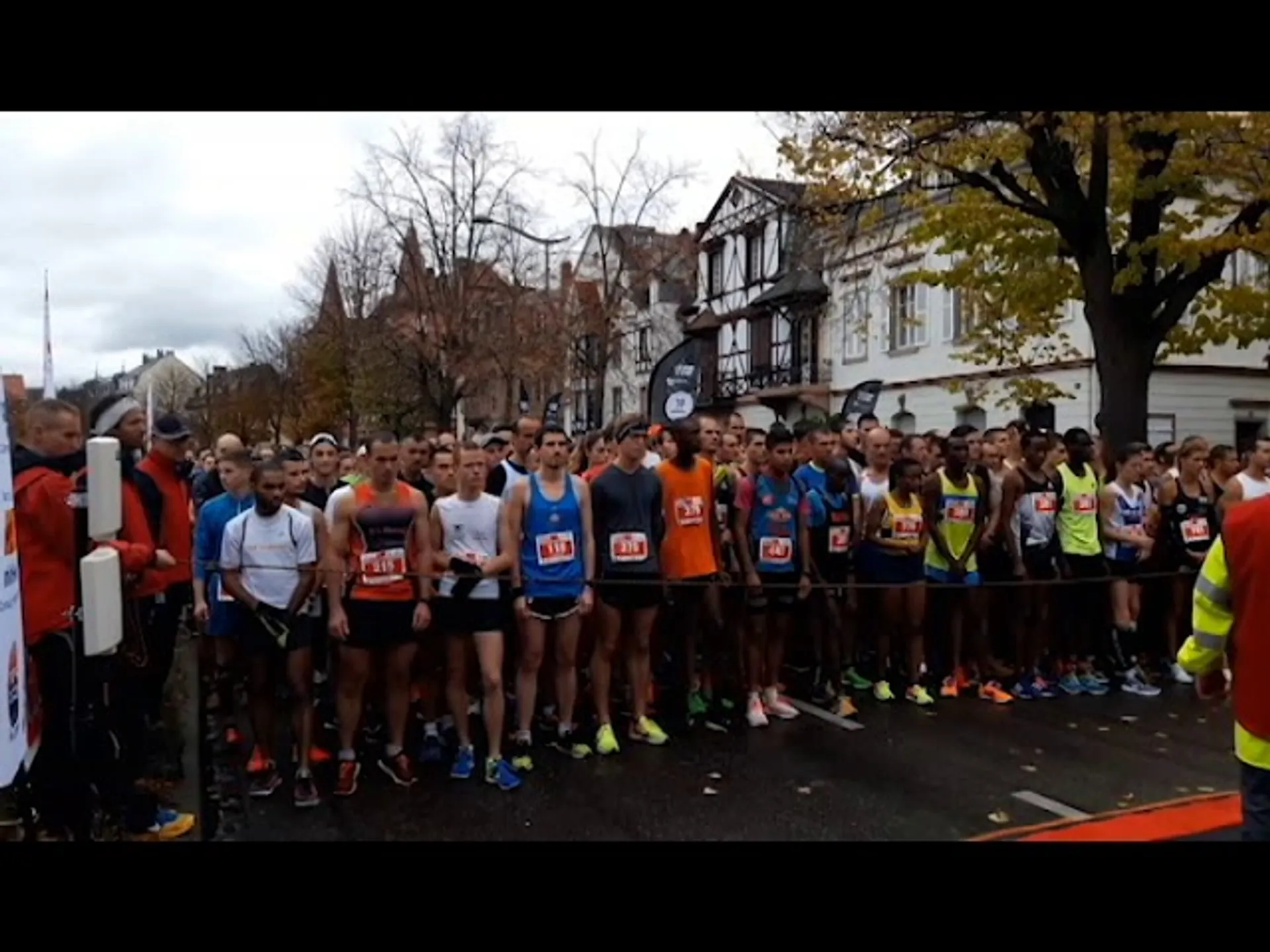 The image shows a group of runners lined up at the start line of a race