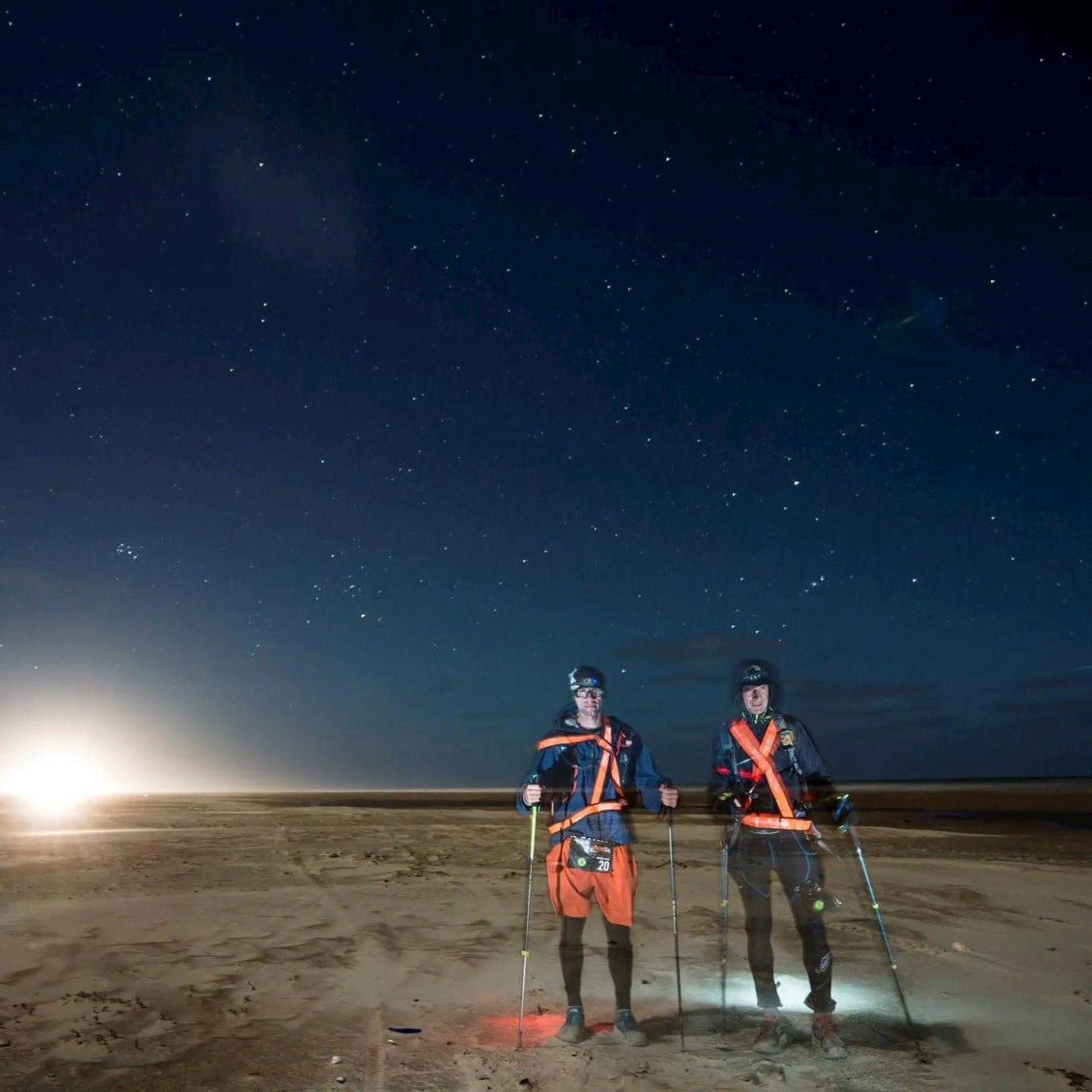 The image shows two individuals standing on a barren landscape at night or during twilight under