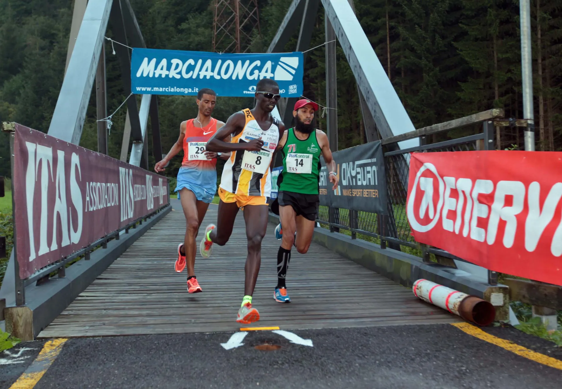 The image depicts three athletes engaged in a running competition. They are crossing a bridge