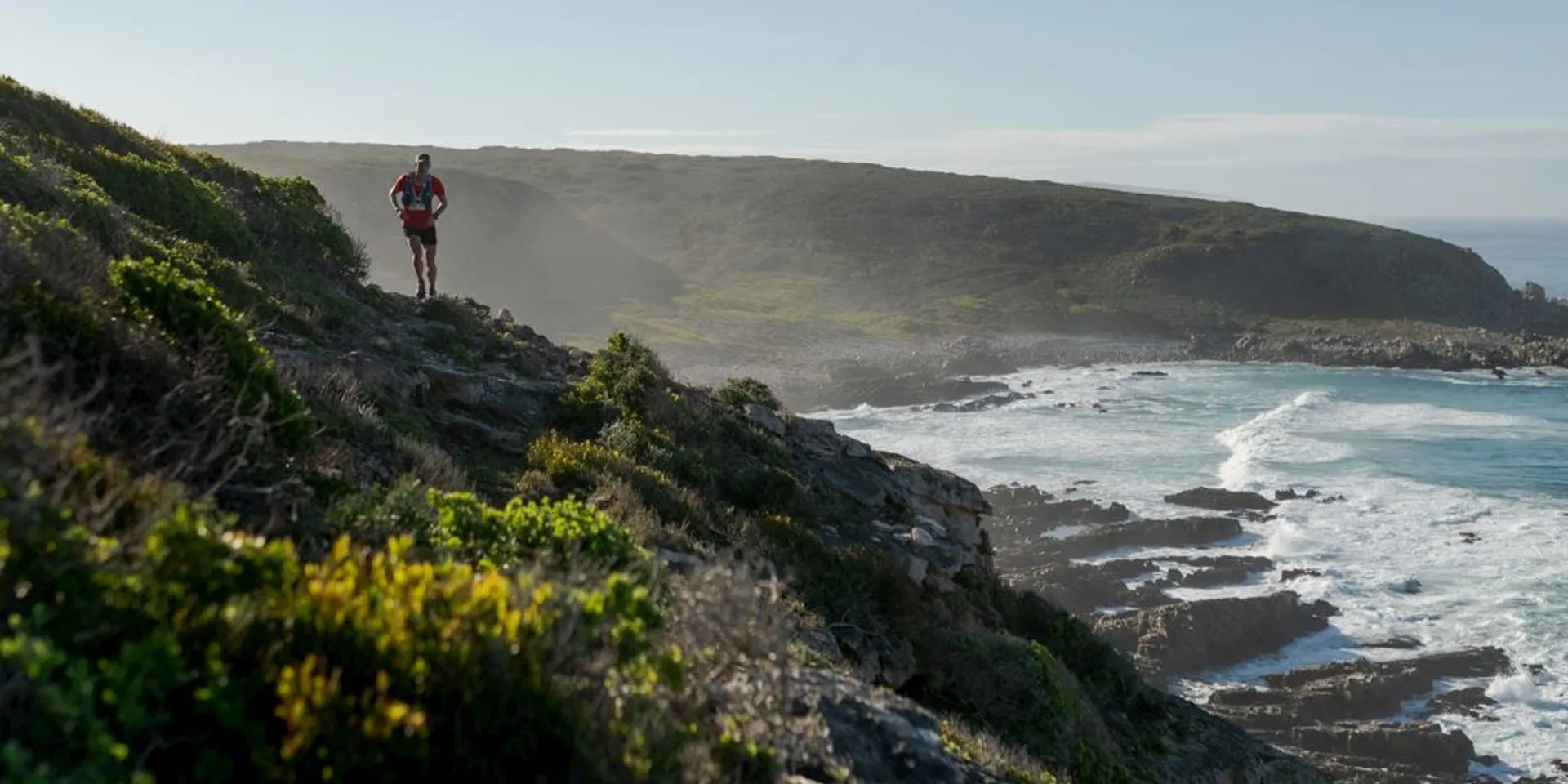 The image features a coastal landscape with a person on a trail. The person appears