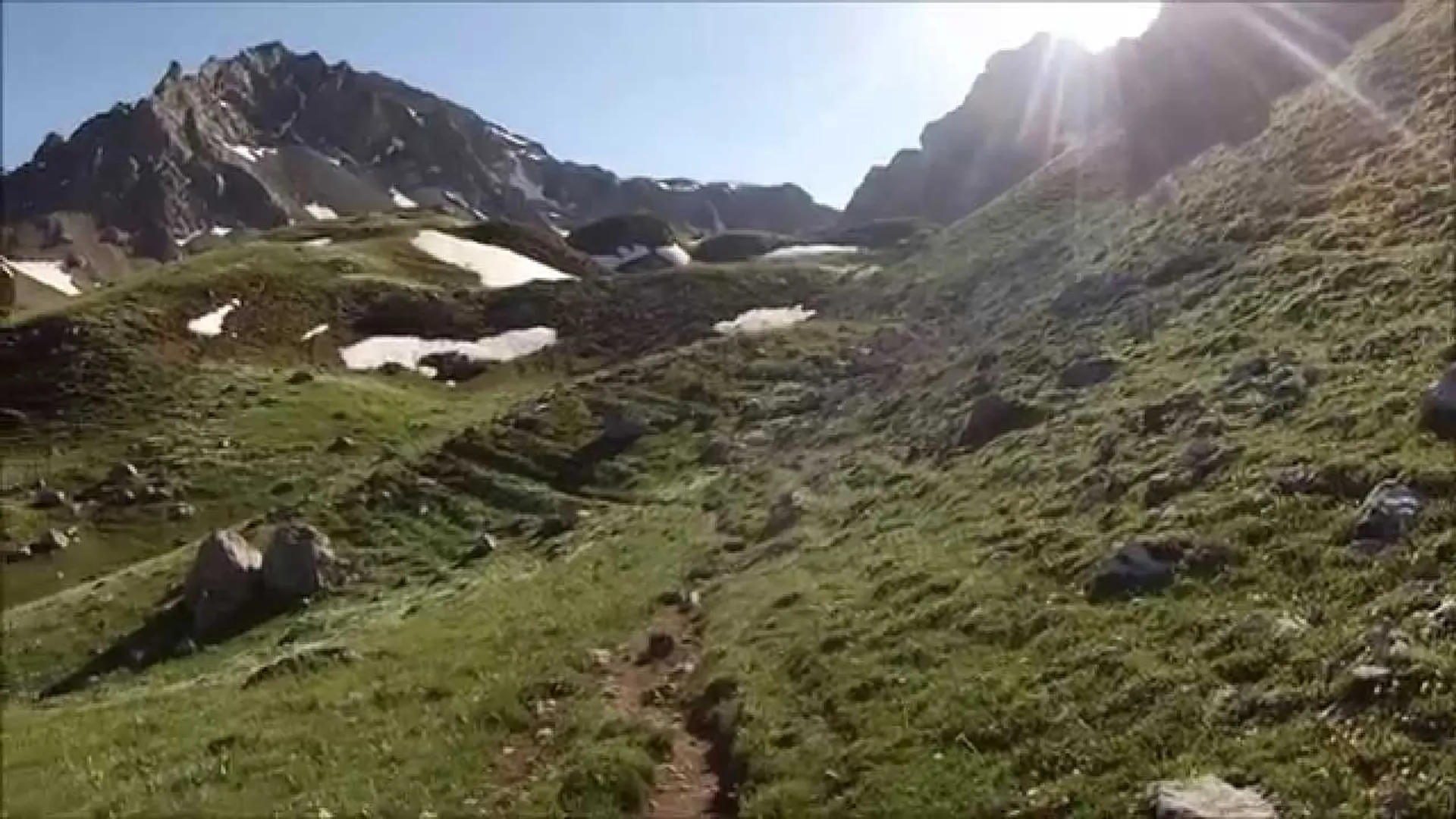 The image depicts a mountainous landscape with a hiking trail. There's green vegetation