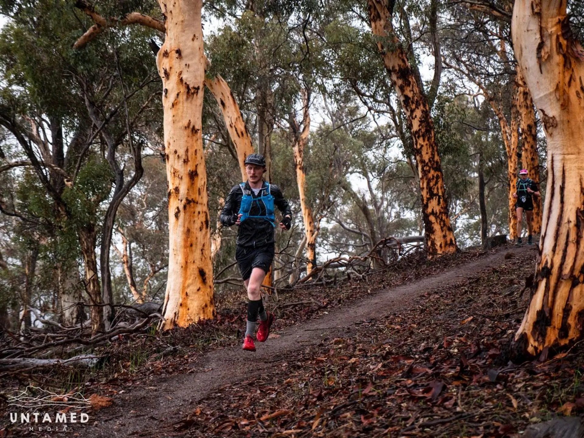 This image depicts a trail running scene. A person is seen running along a dirt