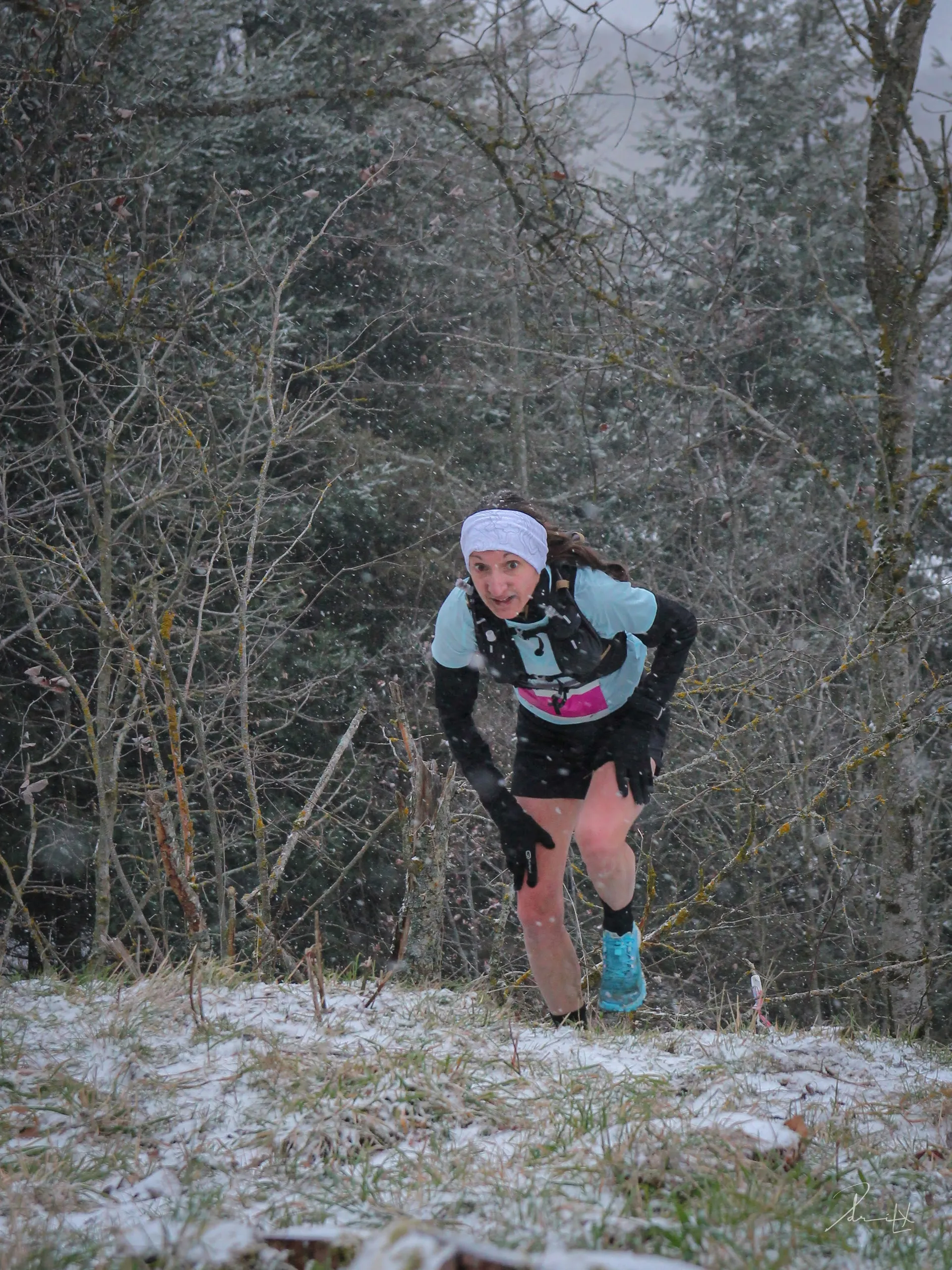 The image shows a person running uphill in a natural setting with some snow on the