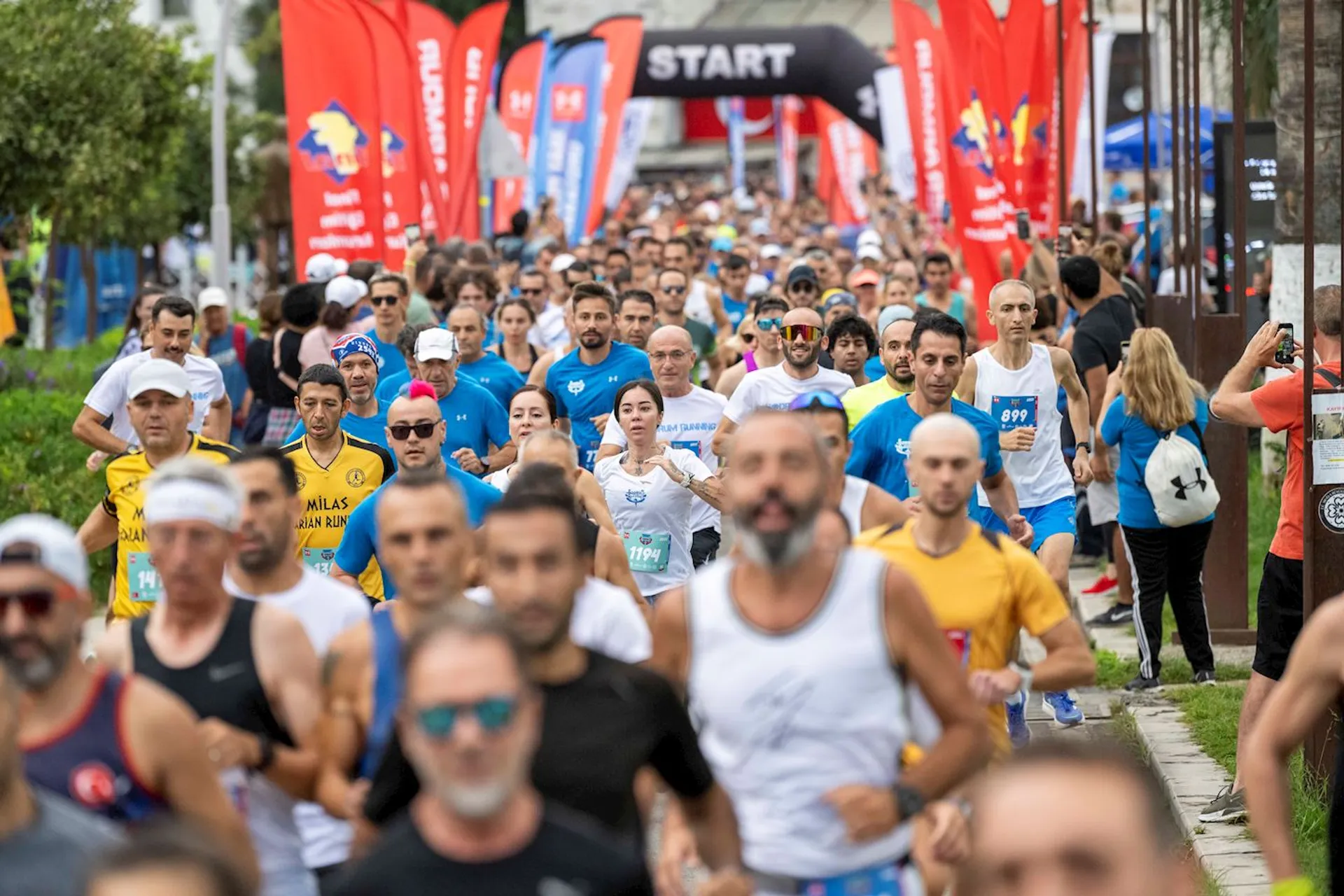 The image depicts a large group of people participating in a running event. The participants