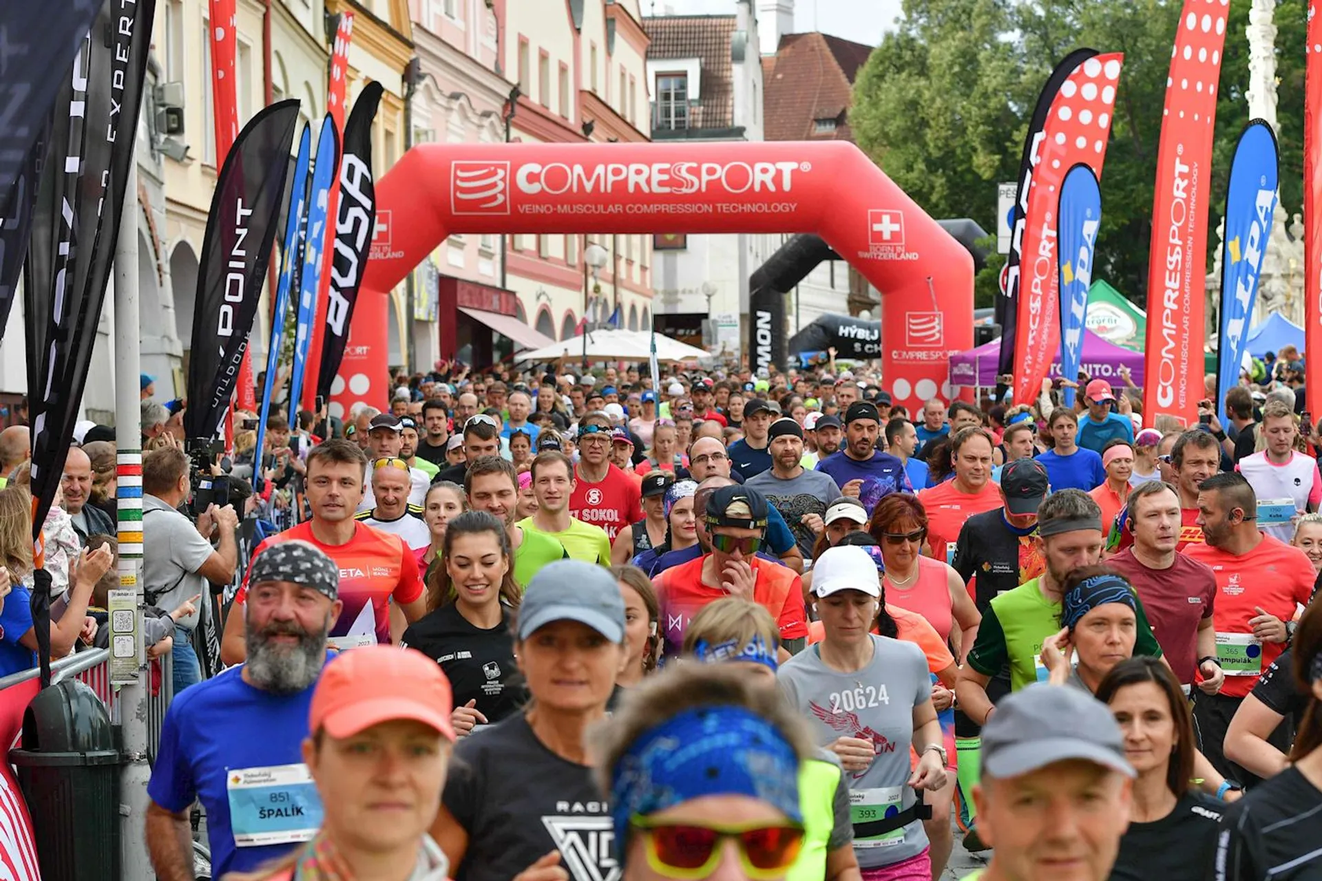 The image depicts a large group of people participating in a running event. They are