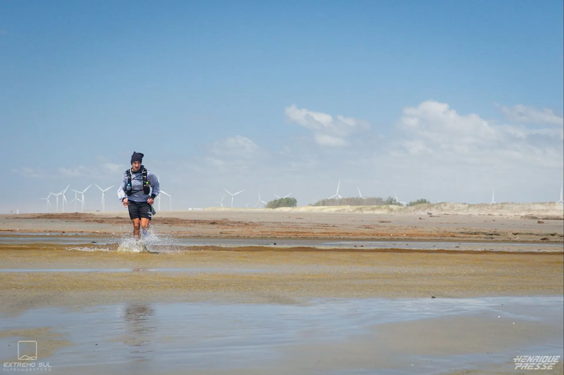 The image shows a person walking through shallow water on what appears to be a sandy