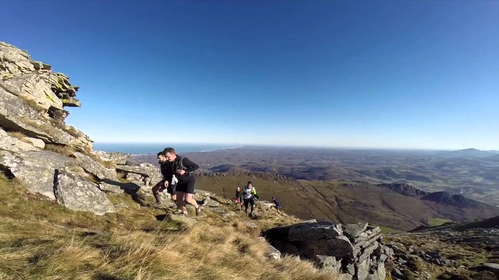 The image shows a person hiking on a mountain trail. They are near a rocky