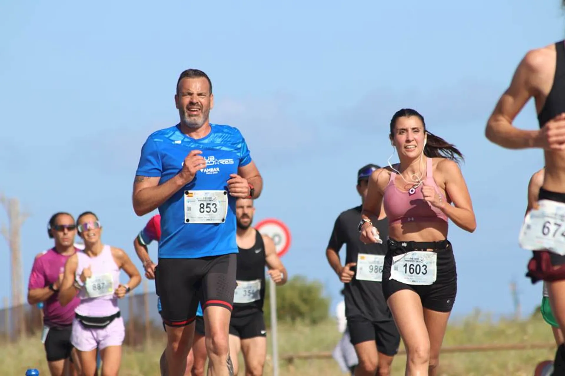 The image shows a group of people running in a race. They are wearing athletic clothing and bib numbers. The background suggests an outdoor setting, possibly during a marathon or a fun run.