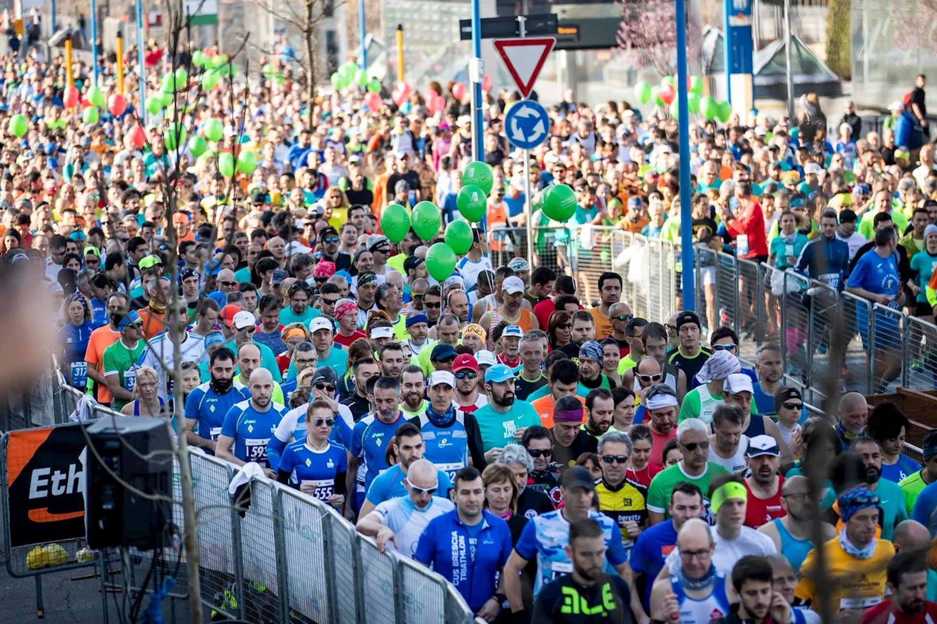 The image shows a large group of runners gathered at the start of a road race